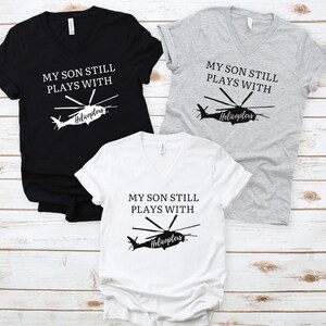 May include: Three V-neck t-shirts with a black helicopter graphic and the text "My son still plays with helicopters". The shirts are black, white, and heather gray.