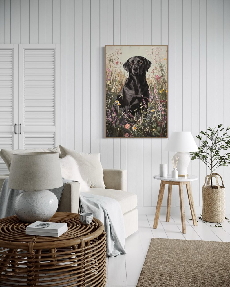 Pode incluir: Um labrador retriever preto sentado em um campo de flores silvestres. O c&atilde;o est&aacute; olhando diretamente para a c&acirc;mera. A pintura &eacute; emoldurada e pendurada em uma parede branca em uma sala de estar.