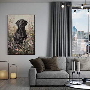 Pode incluir: Um c&atilde;o Labrador Retriever preto sentado em um campo de flores silvestres. O c&atilde;o est&aacute; olhando diretamente para a c&acirc;mera. A imagem est&aacute; emoldurada em uma moldura preta e est&aacute; pendurada em uma parede de uma sala de estar.