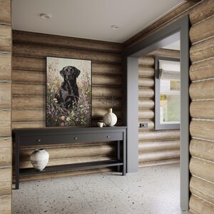 Pode incluir: Um labrador retriever preto est&aacute; sentado em um campo de flores silvestres, emoldurado em uma moldura preta. A imagem est&aacute; pendurada em uma parede de um corredor de uma cabana de madeira. Uma mesa de consola de madeira escura com tr&ecirc;s gavetas e uma prateleira inferior fica abaixo da imagem. Um vaso de cer&acirc;mica branco com um design floral fica sobre a mesa, junto com um vaso de cer&acirc;mica branco menor.