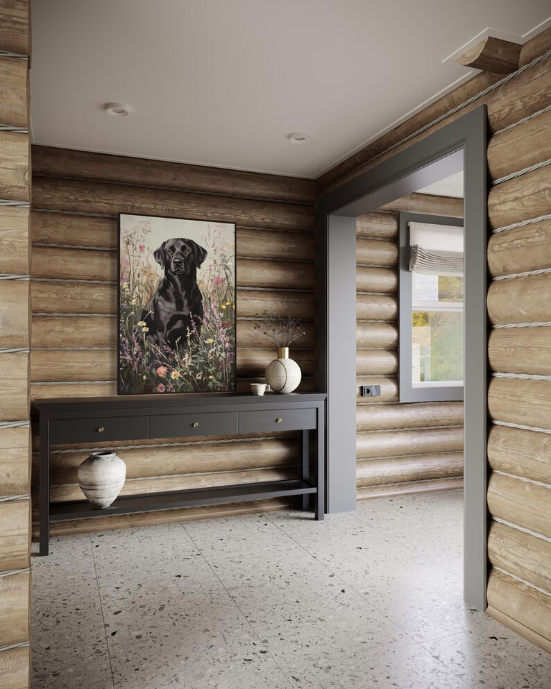 Pode incluir: Um labrador retriever preto est&aacute; sentado em um campo de flores silvestres, emoldurado em uma moldura preta. A imagem est&aacute; pendurada em uma parede de um corredor de uma cabana de madeira. Uma mesa de consola de madeira escura com tr&ecirc;s gavetas e uma prateleira inferior fica abaixo da imagem. Um vaso de cer&acirc;mica branco com um design floral fica sobre a mesa, junto com um vaso de cer&acirc;mica branco menor.