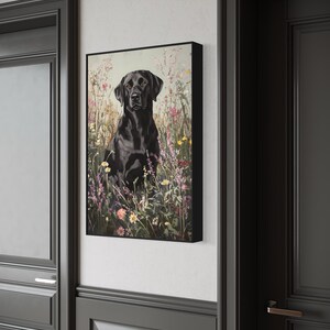 Pode incluir: Um c&atilde;o Labrador Retriever preto sentado em um campo de flores silvestres. O c&atilde;o est&aacute; olhando diretamente para a c&acirc;mera. As flores s&atilde;o rosa, roxo e branco.