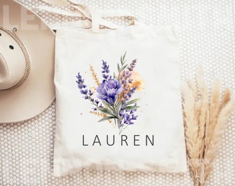 May include: A white tote bag with a floral design featuring purple and yellow flowers. The bag has the name "LAUREN" printed in black at the bottom.