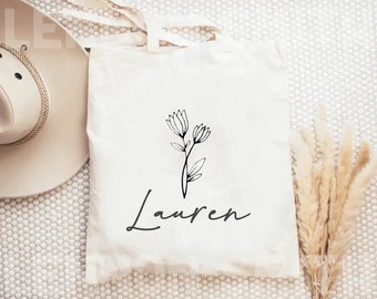 May include: White tote bag with black floral design and the name "Lauren" printed on the front.