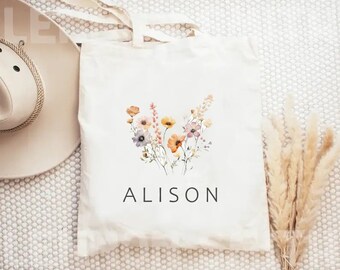 May include: A white tote bag with a floral design in shades of orange, yellow, and purple. The bag has the name "ALISON" printed in black at the bottom.
