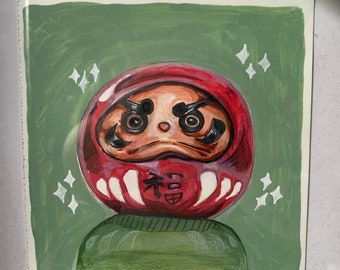 Könnte beinhalten: Eine handgemalte Illustration einer roten japanischen Daruma-Puppe mit weißen Akzenten und einem schwarzen Gesicht. Die Puppe trägt einen grünen Pullover und ist von weißen Glitzerpunkten auf grünem Hintergrund umgeben.