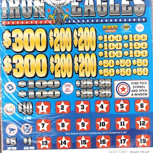 May include: A blue and white scratch-off ticket titled "Iron Eagles" with an eagle graphic. The ticket features various prize amounts and the text "Find this symbol and open a window."