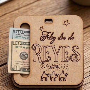 Puede incluir: Un soporte cuadrado de madera de color marrón claro con una ranura para dinero. La parte frontal presenta el texto grabado a láser Feliz dia de REYES, dos estrellas, una estrella fugaz y tres camellos. Se insertan un billete de diez y cien dólares.