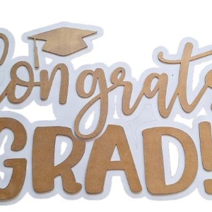 Puede incluir: Un letrero recortado con el texto Congrats GRAD! en un acabado mate de color tostado con un borde blanco. Sobre la palabra Congrats, se sitúa un icono de birrete de graduación de color tostado. Las letras combinan cursiva y bloque.