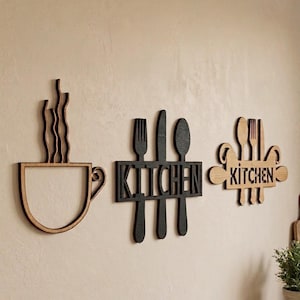 Puede incluir: Tres piezas de arte mural de madera: una taza de café marrón claro con vapor, un recorte negro con tenedor, cuchillo y cuchara con la palabra KITCHEN, y un letrero marrón claro con iconos de cubiertos y la palabra KITCHEN.