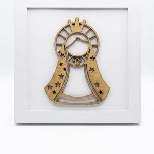 May include: A wooden religious wall art piece featuring a stylized figure with a crown and star-shaped accents. The artwork is set within a white square frame, creating a clean and modern aesthetic. The figure is a light brown color.