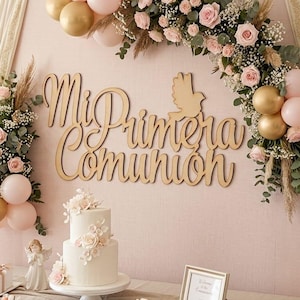 以下が含まれることがあります： 金色の木製文字「Mi Primera Comunión」と鳩のアイコンをあしらった壁面装飾。ピンクとゴールドのバルーン、ユーカリ、バラのアーチで囲まれ、2段の白いケーキとフラワーアレンジメントが添えられています。