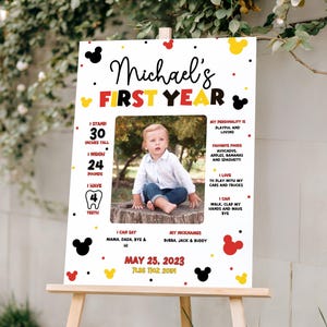 May include: A personalized first birthday sign on an easel. The sign features a photo of a baby and details like height (30 inches), weight (24 pounds), and favorite foods. The design includes Mickey Mouse-themed accents.