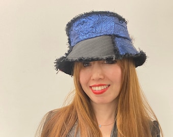 Puede incluir: Una mujer con una chaqueta de cuero negra y un sombrero de cubo azul y negro con borde deshilachado.