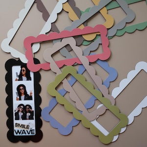 May include: A collection of rectangular photo booth frames with scalloped edges in various colors including pink, blue, green, yellow, and white. One black frame contains a vertical strip of three photos featuring a person and the text SMILE WAVE.