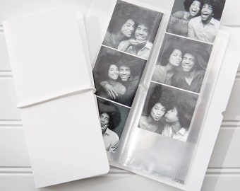 Puede incluir: Un álbum de fotos blanco con un bolsillo de plástico transparente en la parte delantera. El bolsillo contiene una tira de fotos de cabina de fotos en blanco y negro de una pareja.