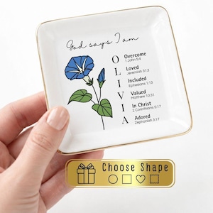 May include: A square white ceramic trinket dish with a gold-toned rim. The center features a blue morning glory flower illustration, the text God says I am, and the name OLIVIA vertically aligned with religious verses for each letter.