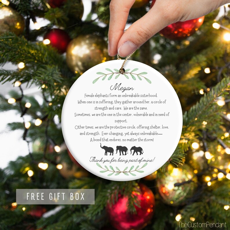 Peut inclure: Une boule de No&euml;l ronde en c&eacute;ramique blanche avec un motif de feuilles vertes et le nom "Megan" &eacute;crit en noir. La boule pr&eacute;sente une citation sur les &eacute;l&eacute;phantes femelles formant une fraternit&eacute; ind&eacute;fectible, avec trois &eacute;l&eacute;phants noirs en silhouette en bas. Le texte dit "Merci d'&ecirc;tre une partie de moi !"