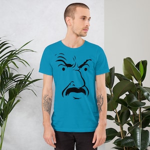 May include: A turquoise t-shirt featuring a bold black graphic of a stern-looking face with a large mustache. The graphic is centered on the front of the shirt. The shirt is made of a soft material.