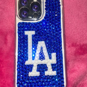 May include: A clear phone case with a blue and white LA logo. The case is covered in blue rhinestones.