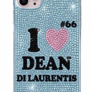 May include: A light blue phone case covered in small sparkling crystals. The design features a black letter I, a pink crystal heart, and the black text DEAN DI LAURENTIS with the number #66 in black, all set against the light blue crystal background.