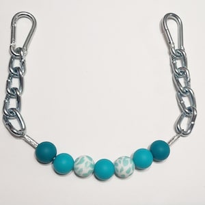 Puede incluir: Una cadena plateada con dos clips plateados en cada extremo. La cadena tiene seis cuentas de color azul turquesa, dos cuentas sólidas y cuatro cuentas con un patrón blanco.