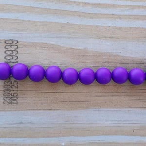 Puede incluir: Una cadena de cuentas moradas con eslabones metálicos plateados en cada extremo. La cadena está hecha de 9 cuentas redondas y 2 eslabones metálicos.