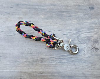 May include: A keychain featuring a braided loop made of black and rainbow-colored paracord. The cord is secured with a knot to a silver-toned metal swivel lobster clasp, providing a functional attachment point for keys or other small personal items.