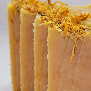 May include: Four bars of handmade soap with a light brown color and a textured surface. The soap is topped with dried yellow flower petals.