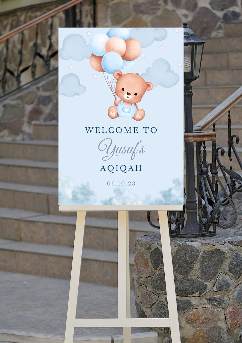 May include: A blue and white welcome sign with a cartoon bear holding balloons. The sign says "Welcome to Yusuf's Aqiqah 06.10.23".
