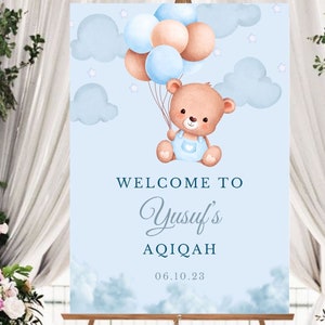 May include: A blue and white welcome sign with a cartoon bear holding balloons. The sign says "Welcome to Yusuf's Aqiqah 06.10.23".