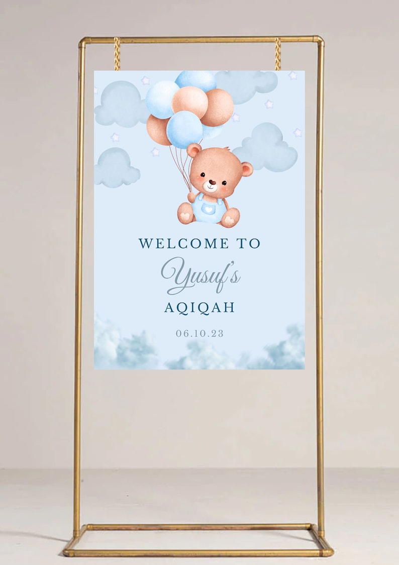 May include: A blue and white welcome sign with a teddy bear holding balloons. The sign says "Welcome to Yusuf's Aqiqah 06.10.23".