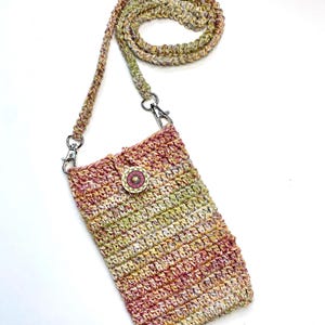 May include: A handmade crochet phone crossbody bag in shades of pink, yellow, and green. The bag features a decorative wooden button and a matching crochet strap with silver-tone metal clasps. The bag is designed to hold a phone and other small items.