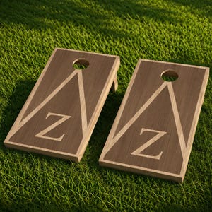 Könnte beinhalten: Zwei rechteckige Cornhole-Boards aus Holz mit einer natürlichen Holzmaserung. Jedes Board hat ein kreisförmiges Loch im oberen Bereich und eine große, helle dreieckige Umrandung, die einen markanten Großbuchstaben Z in der Mitte umschließt.