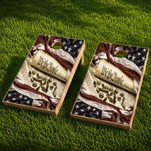 May include: Two rectangular cornhole boards featuring a printed design of the United States flag, a parchment document with the text We the People, and scattered metallic bullet casings. Each board has a circular hole near the top edge.
