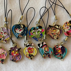 May include: A set of ten colorful character charms with black string phone charms. The charms feature characters from the animated series Helluva Boss.
