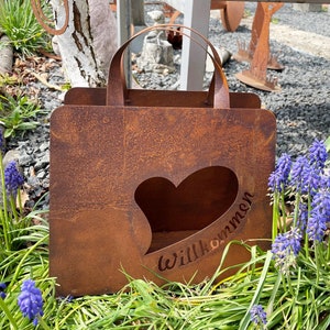 Può includere: Decorazione da giardino in metallo marrone arrugginito a forma di borsa della spesa. Presenta un ritaglio a forma di cuore e la parola "Willkommen" tagliata nel metallo. La borsa ha due manici arcuati.