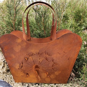 May include: A rusty metal planter shaped like a shopping bag with a dandelion design. The planter is brown and has a handle.