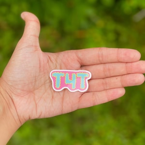May include: Pink sticker with a blue and yellow outline, featuring the text "TYT" in a bubbly font.