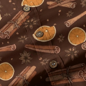 May include: A brown button-down shirt featuring a repeating pattern of orange slices, cinnamon sticks tied with twine, and star anise. The garment has a vertical placket with three visible round, textured brown buttons centered on the fabric.