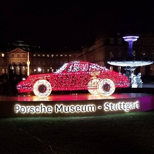 May include: A red car made of lights, with the words "Porsche Museum - Stuttgart" on a sign in front of it.