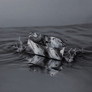 May include: A black and white marbled clutch purse floats in water, creating a splash. The purse has a flap closure with a single black button. The water's surface reflects the purse's design, and the background is a muted gray.