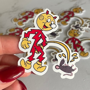 May include: A red and yellow cartoon character with a lightning bolt design is peeing on a small gray mouse. The character is wearing a red suit and has a yellow head with a lightning bolt on top. The mouse is lying on its back with its legs in the air. The character is holding a hose that is spraying water on the mouse.