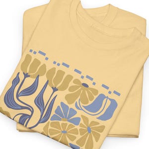 May include: A folded yellow t-shirt with a floral print in shades of blue and yellow. The print features stylized flowers and leaves.