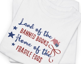 Op de afbeelding: Wit T-shirt met een blauwe en rode Amerikaanse vlag afbeelding en de tekst "Land of the Banned Books Home of the Fragile Egos".