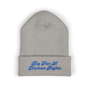 May include: A gray beanie with the phrase "Big Fan Of Human Rights" embroidered in blue. The beanie is made of a soft, knitted material and has a folded brim. The text is in a retro font.