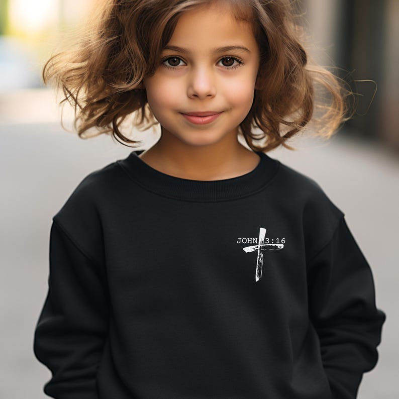K&ouml;nnte beinhalten: Schwarzer Pullover mit einem wei&szlig;en Kreuz und dem Text "JOHN 3:16" auf der Vorderseite.