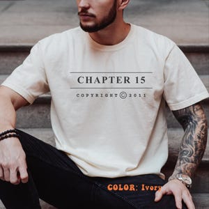 May include: An ivory short-sleeve t-shirt featuring the text CHAPTER 15 centered on the chest between two horizontal lines, with the text COPYRIGHT © 2011 printed directly below. The shirt has a crew neckline and a standard fit design.