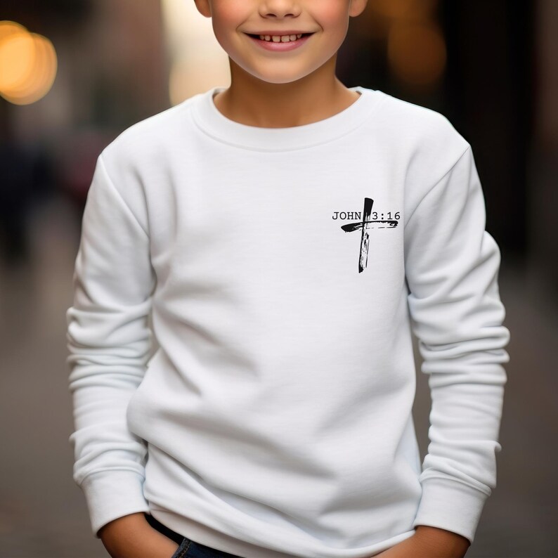 K&ouml;nnte beinhalten: Wei&szlig;er Langarm-Pullover mit einem schwarzen Kreuz und dem Text "JOHN 3:16" auf der Vorderseite.