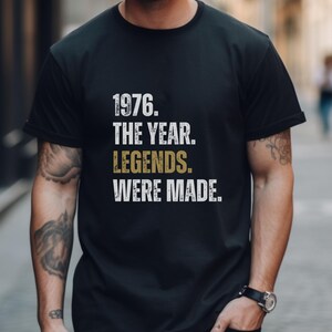 May include: Black t-shirt with white and gold text that reads "1976. THE YEAR. LEGENDS. WERE MADE." The shirt has a crew neck and short sleeves. The text is in a bold, distressed font.